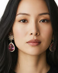 Aretes Bloom Drop de Queens Candy con diseño floral, zirconias y gota de cristal fucsia en baño dorado.