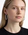Modelo luciendo aretes hoop Queens Candy de 26mm en cobre con baño plateado y zirconias brillantes