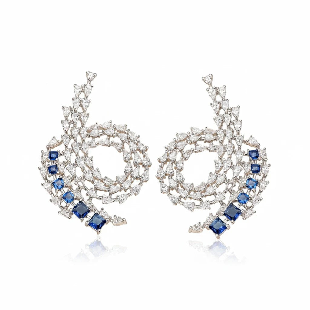 Aretes Queens Candy de cobre con baño de rodio, zirconias azules tipo zafiro y perlas simuladas en diseño espiral.
