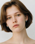 Modelo luciendo pendientes de aro Queens Candy de plata bañada en oro con zircones turquesa en corte baguette